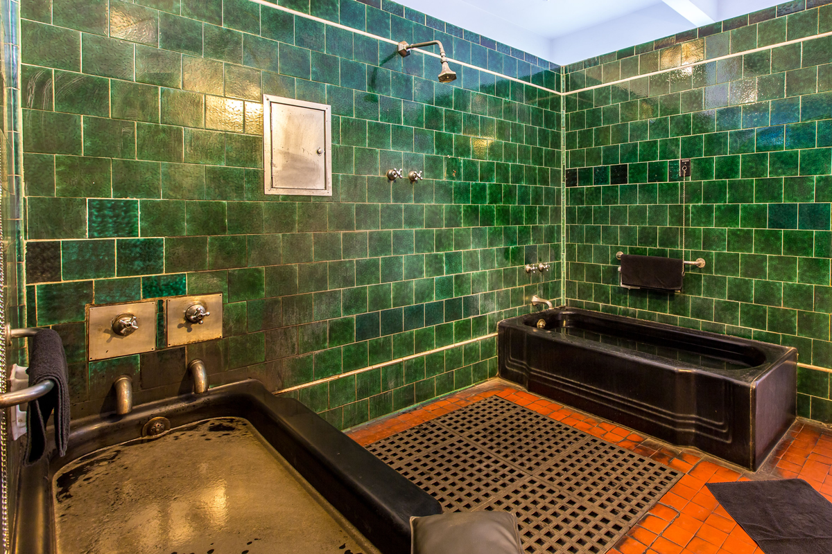 Banheiro com azulejos verde escuros com duas banheiras com banho medicinal.